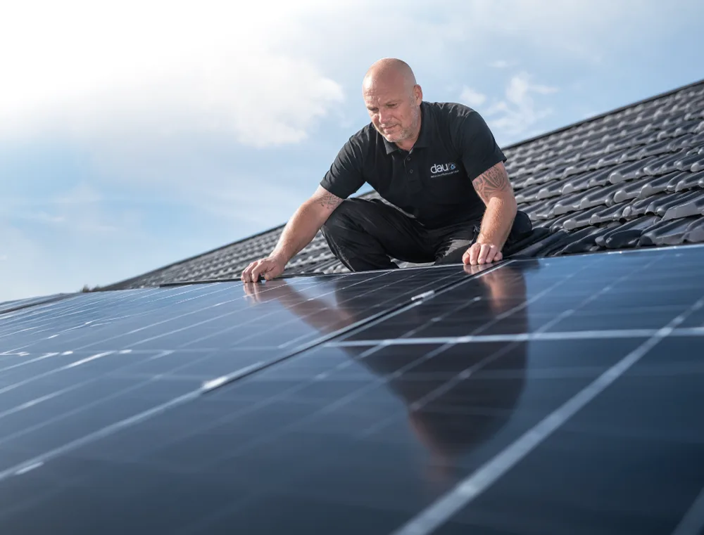 DAU-Mitarbeiter montiert Photovoltaik-Module auf einem Hausdach – Kombination mit Wärmepumpe